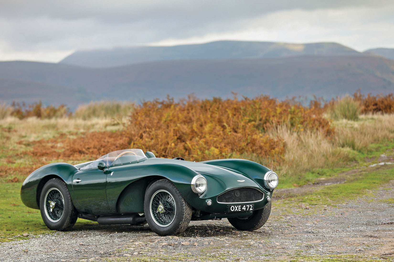 Grüner Aston-Martin-Rennsportwagen der 1950er-Jahre mit Speichenrädern vor herbstlicher Hügellandschaft