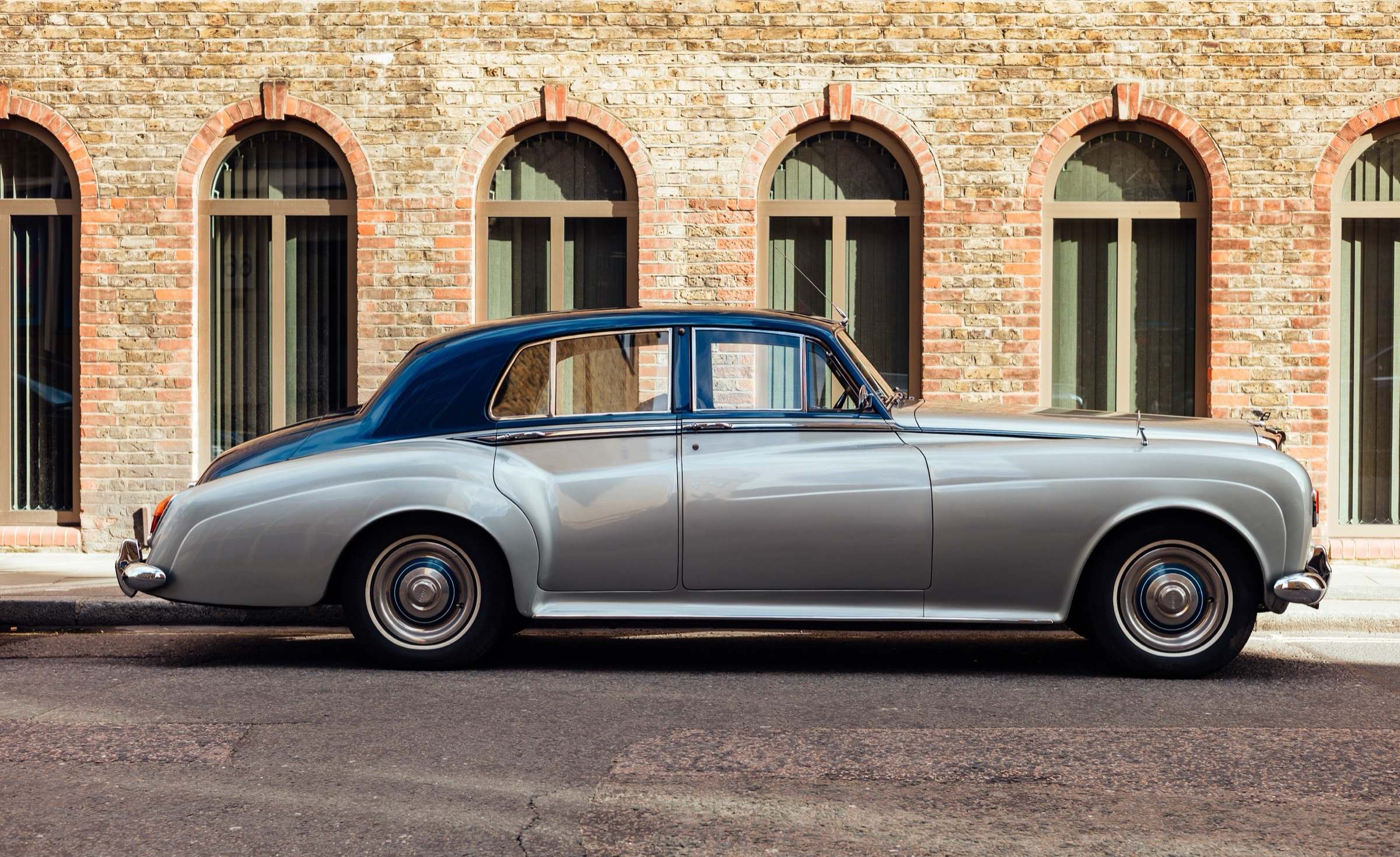 Zweifarbige britische Luxuslimousine der 1950er- oder 60er-Jahre in Silber und Dunkelblau, Seitenansicht vor einer Backsteinfassade